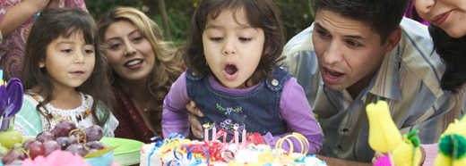 child blowing out birthday candles with family