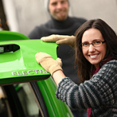 Dark haired woman standing next to green electric car