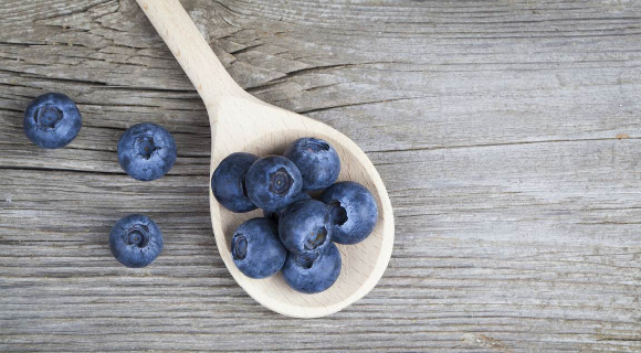 Wooden spoon holding blueberries on wood tabletop