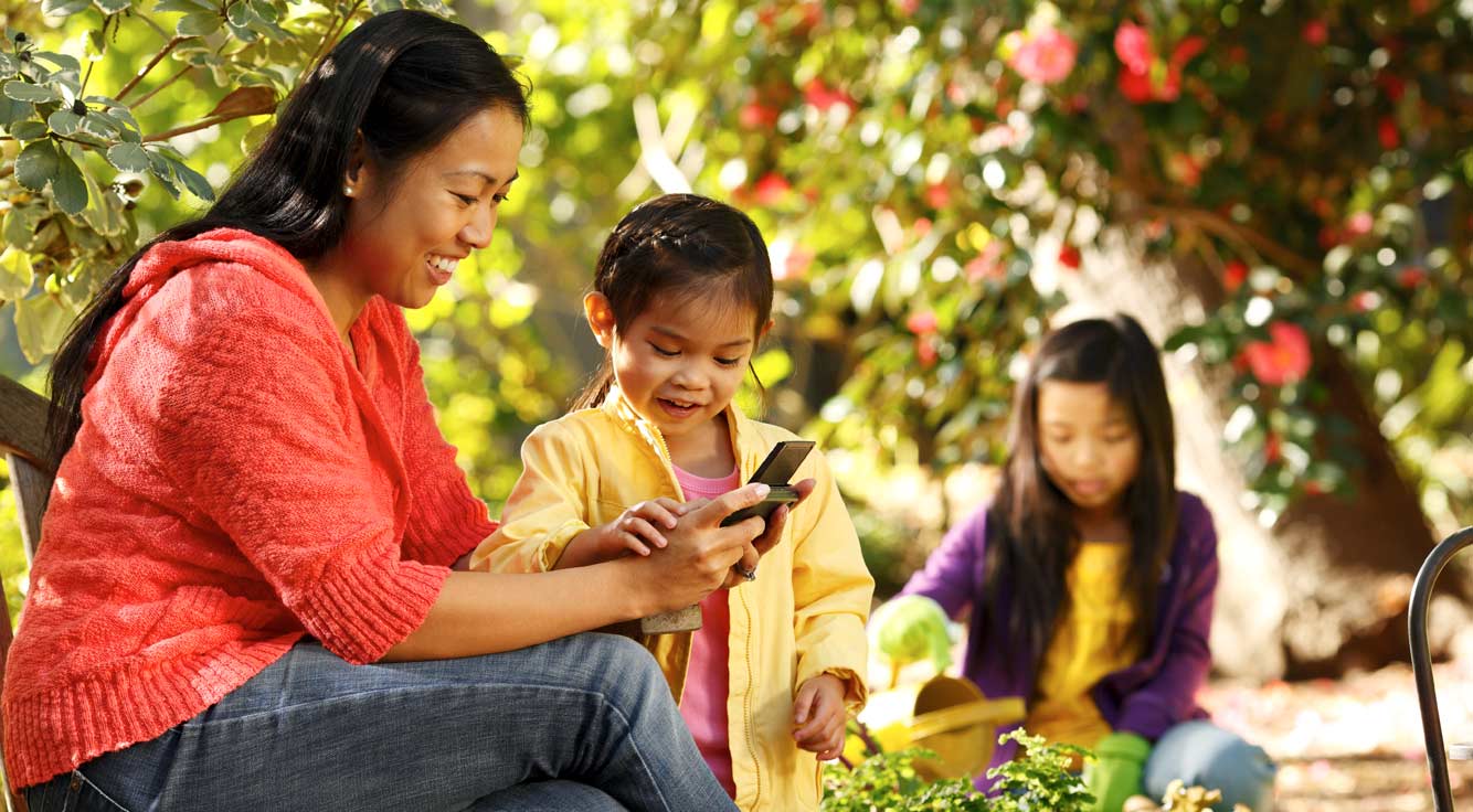 Mother and her child sitting on a garden bench looking at her smart phone.