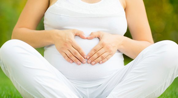 Pregnant woman holding hands over belly in shape of a heart