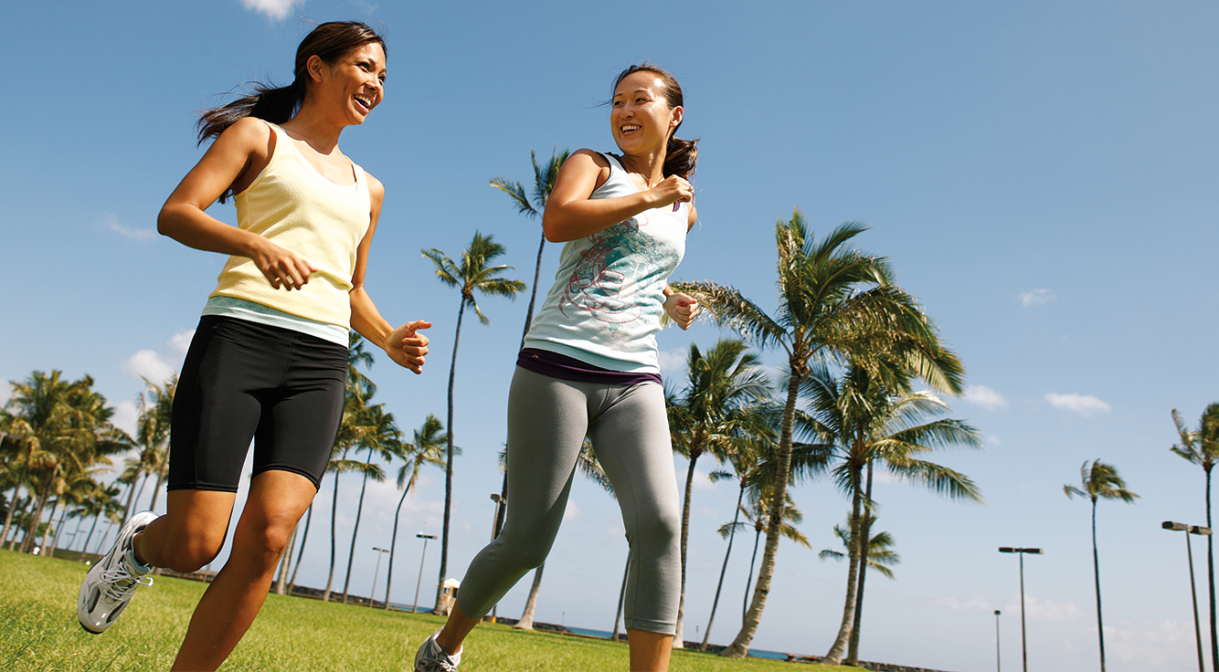 2 smiling women jog past palm trees.