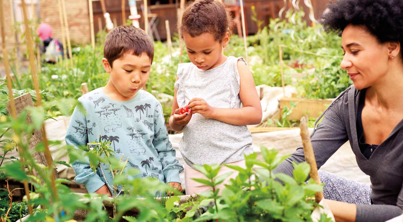 A woman and two small children visit a vegetable garden.