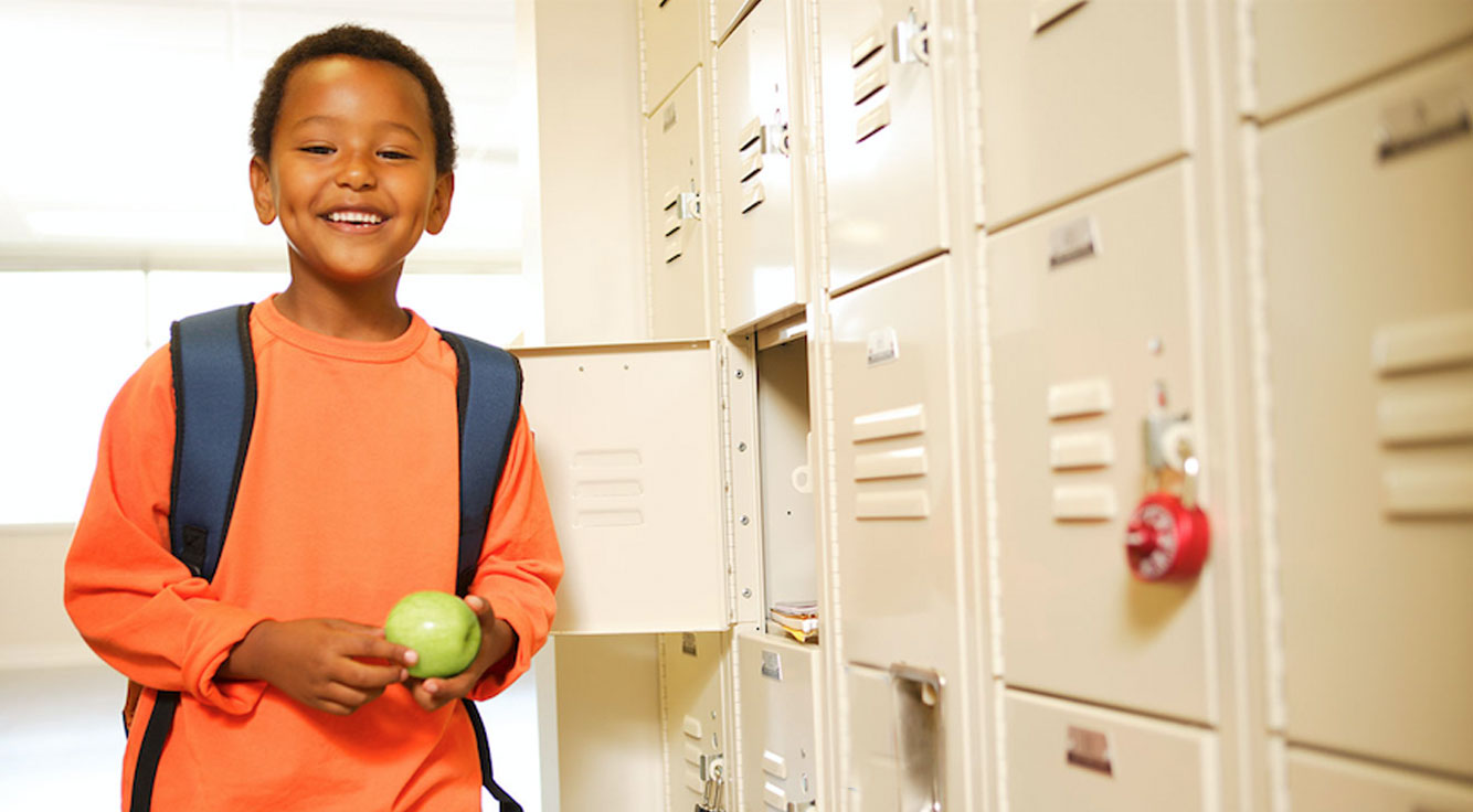 A boy smiles proudly at his school locker.