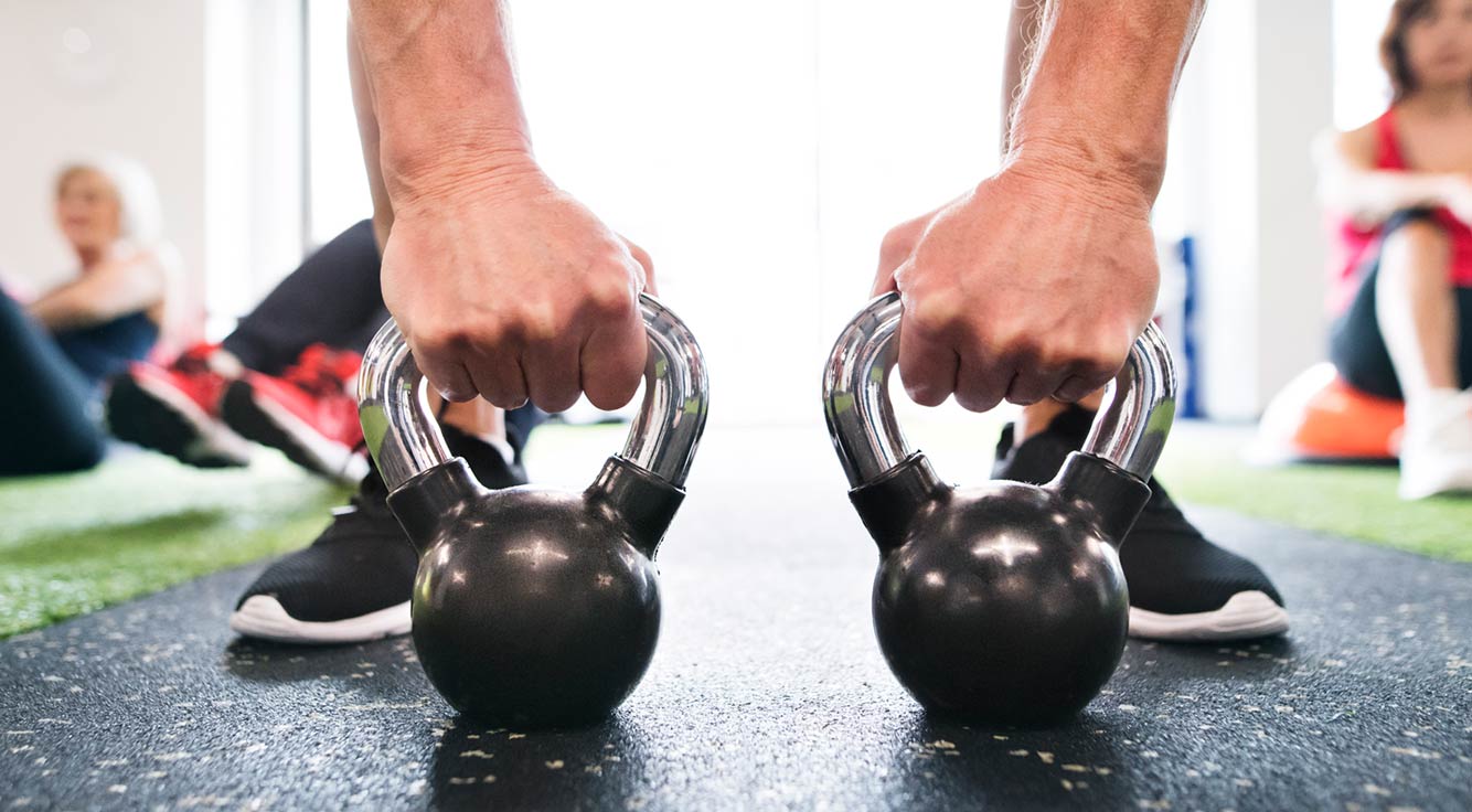 A gym-goer prepares to lift two kettlebell weights.