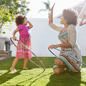 A woman and her children playing with hula hoops and a ball in their backyard.