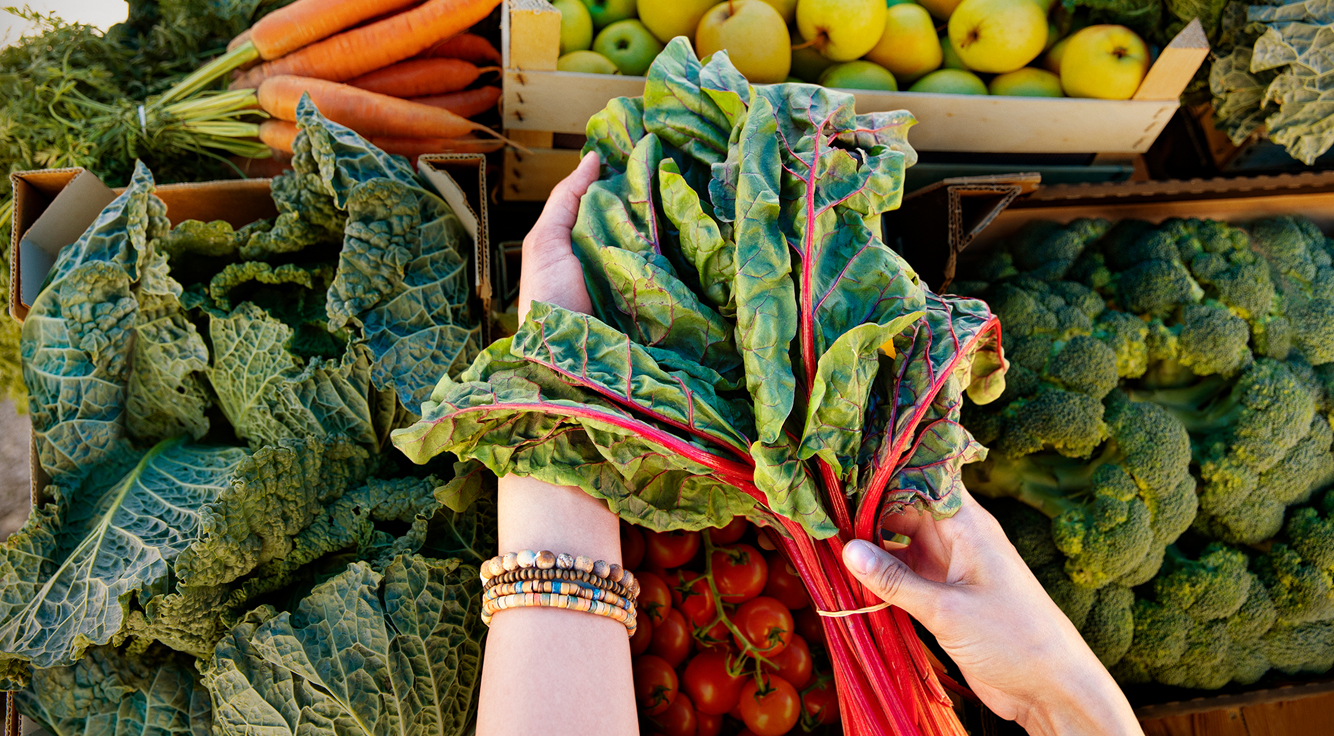 A woman holds a bunch of chard at a farmers market