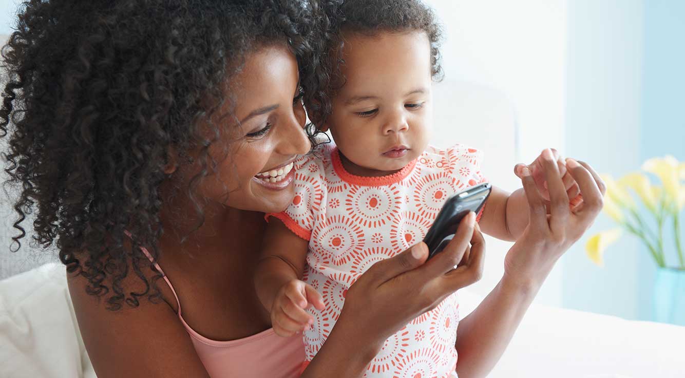 A smiling mother shows her smartphone to her baby