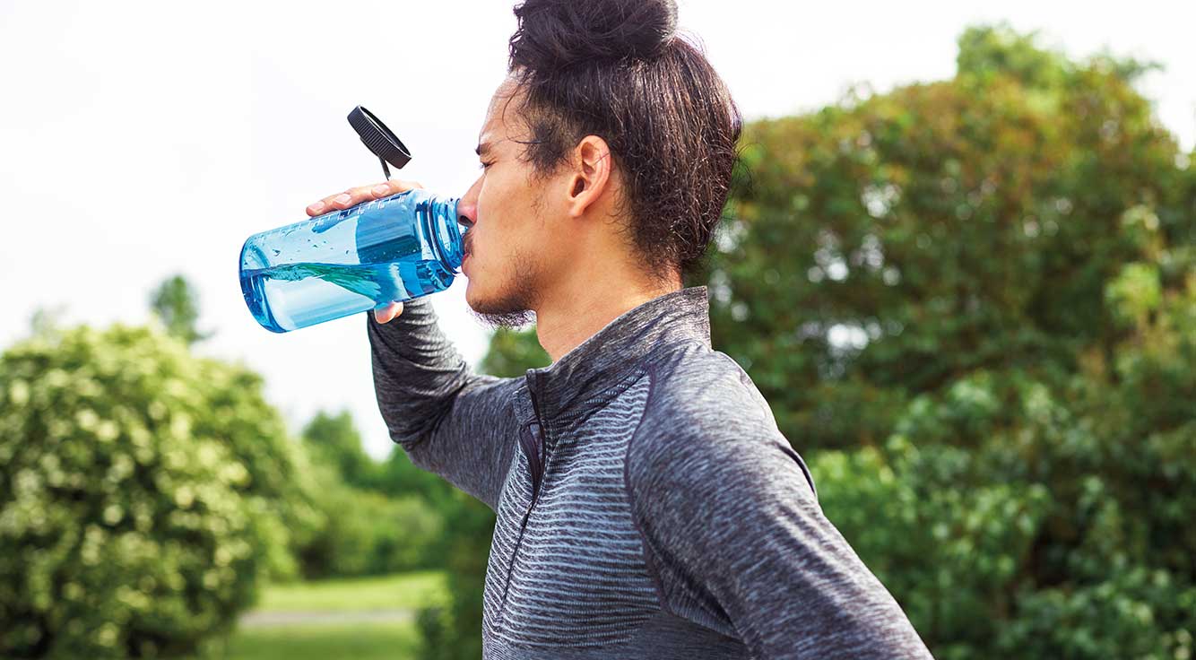 A young man in workout clothes sips from a water bottle.