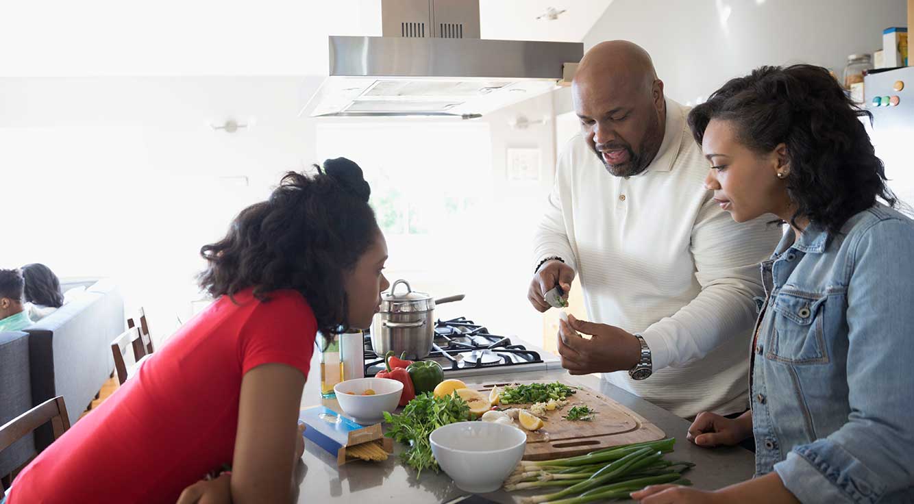 A father shows his two young daughters how to prepare a dish.