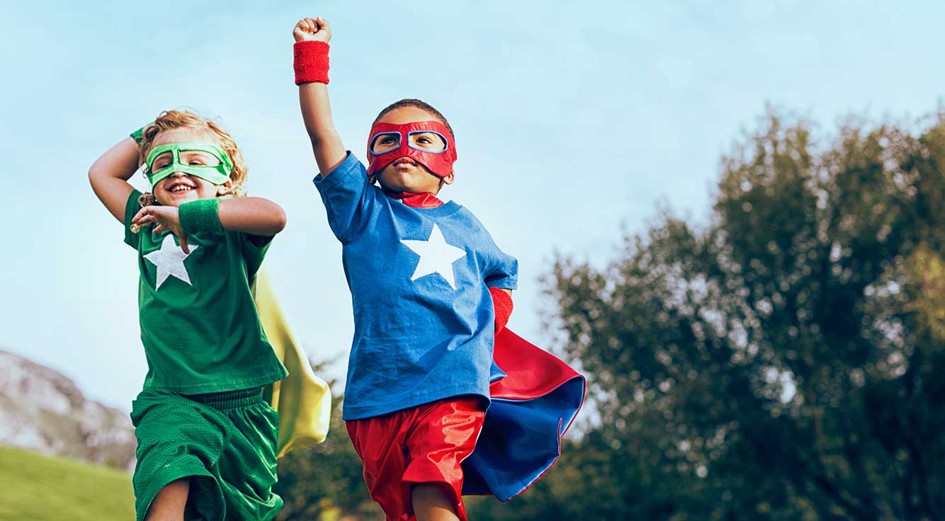 Two children dressed as superheroes play together outside.
