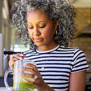 A woman stirs her green juice in the kitchen