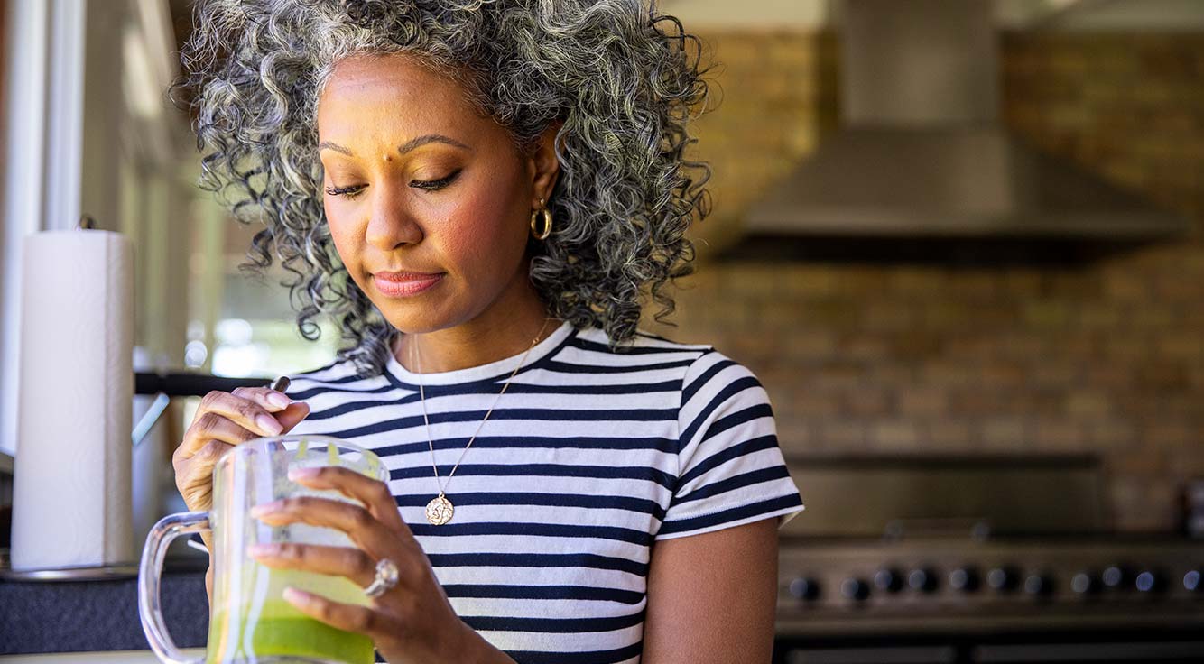 A woman stirs her green juice in the kitchen