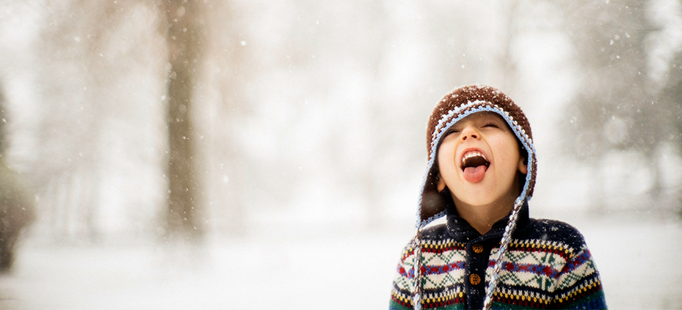 Little boy touching snowflakes with tongue
