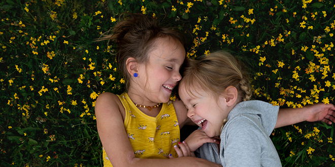 Two young girls laughing while lying on flower covered grass.